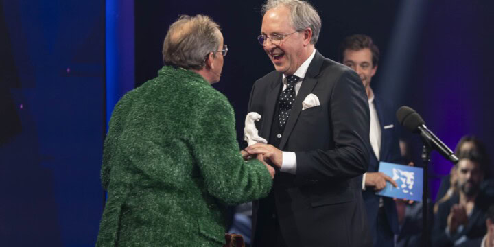 Two men in suits shaking hands at a awards ceremony
