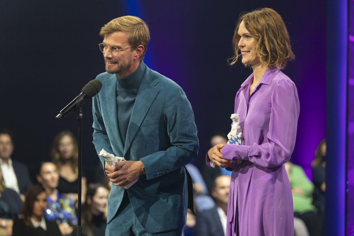 Executive Producer Julia Mehnert (rechts) und Moderator Joko Winterscheidt (links) bei der Preisverleihung. Joko steht am Mikrofon und hält eine Dankesrede.