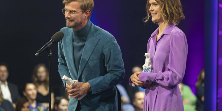 Executive Producer Julia Mehnert (rechts) und Moderator Joko Winterscheidt (links) bei der Preisverleihung. Joko steht am Mikrofon und hält eine Dankesrede.
