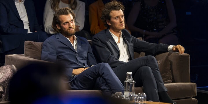 Jono und Benji Bergmann sitzen beim Blauen Panther 2022 auf einer Couch. Im Hintergrund ist vereinzelt das Publikum zu sehen. (c) Medien.Bayern - Ralf Wilschewski