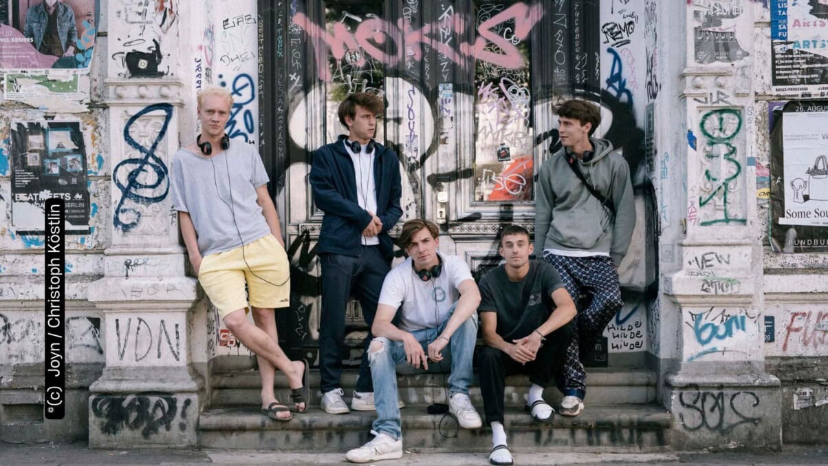 Emil Belton, Oskar Belton, Max Mattis und Leo Fuchs stehen und sitzen vor einer mit Graffitti besprühten Wand (c) Joyn Christoph Köstlin