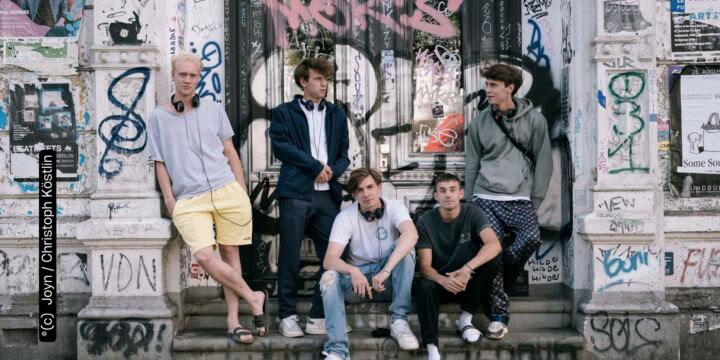 Emil Belton, Oskar Belton, Max Mattis und Leo Fuchs stehen und sitzen vor einer mit Graffitti besprühten Wand (c) Joyn Christoph Köstlin