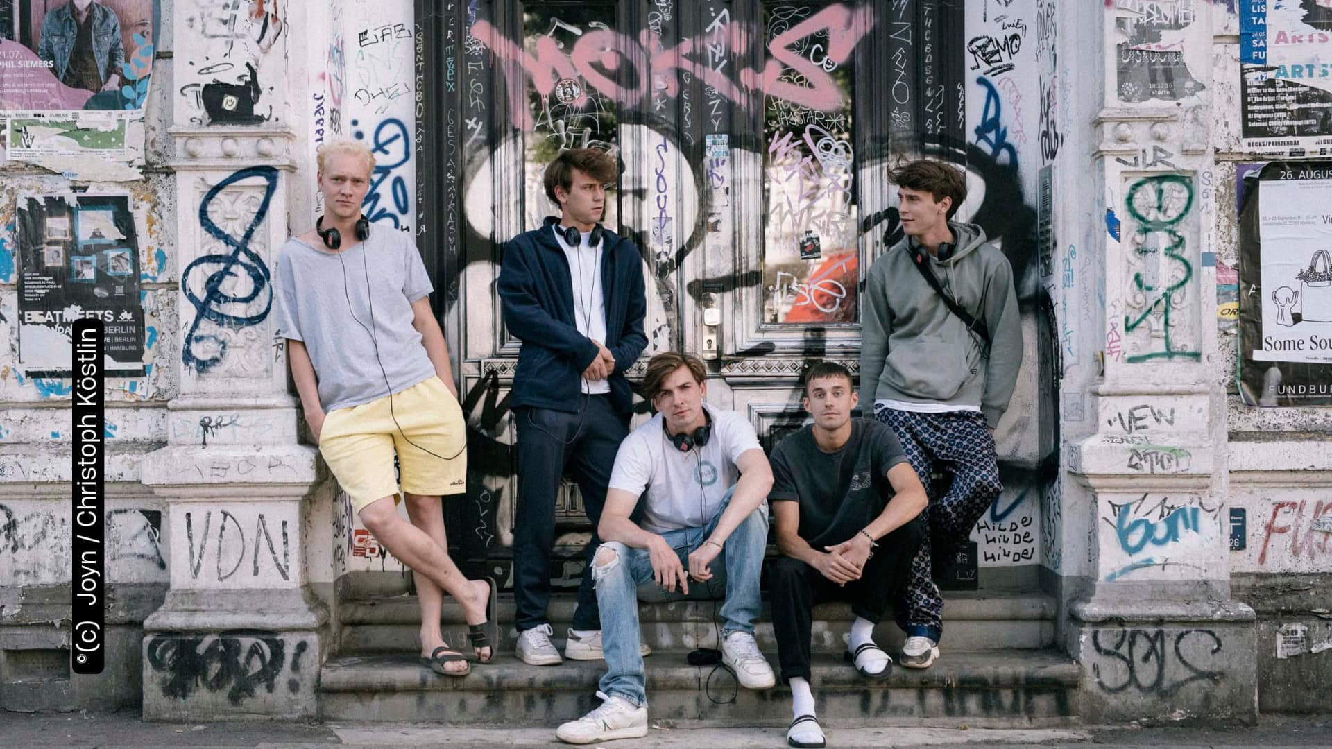 Emil Belton, Oskar Belton, Max Mattis und Leo Fuchs stehen und sitzen vor einer mit Graffitti besprühten Wand (c) Joyn Christoph Köstlin