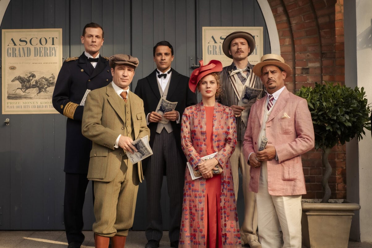 TV & Streaming Tipps Dezember 2025: Sechs Personen in eleganter Kleidung der 1920er Jahre posieren vor einem Eingang mit „Ascot Grand Derby“-Plakaten und halten Rennprogramme in den Händen.