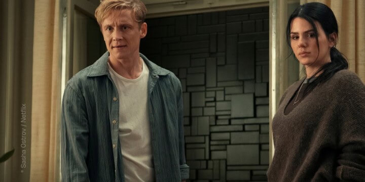 TV & Streaming Tipps im Juli 2025: Ein Mann, gespielt von Matthias Schweighöfer, und eine Frau, gespielt von Ruby O. Fee, stehen in einem Raum. Man sieht Vorhänge an einem Fenster. Das Fenster ist geöffnet. Vor dem Fenster ist keine Landschaft zu sehen, sondern eine schwarze Mauer, gebaut aus unterschiedlich geformten Mauersteinen. Offizielles Pressefoto von „Brick– Kein Weg nach draußen” (Netflix).