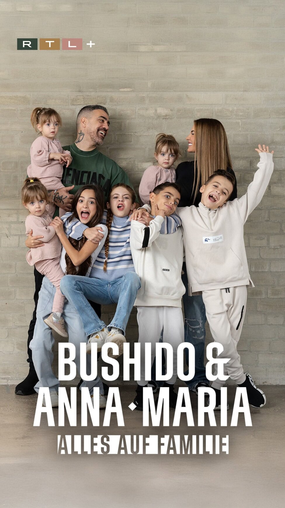 TV & Streaming Tipps im August – Special „Beliebteste Reality-Serie” Plakat zur Serie ‚Bushido & Anna-Maria – Alles auf Familie‘ bei RTL+. Darauf sind Bushido, Anna-Maria und ihre Kinder zu sehen. Sie lachen, kuscheln und stehen eng zusammen vor einer grauen Wand. Unten steht der Serientitel groß in weißer Schrift.