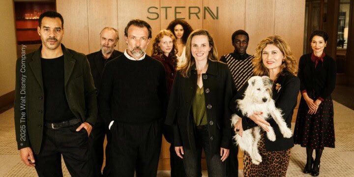 Mehrere Personen stehen im Foyer eines Büros und blicken direkt in die Kamera, sie tragen lockere Businesskleidung. Eine Person hält einen Hund auf dem Arm.