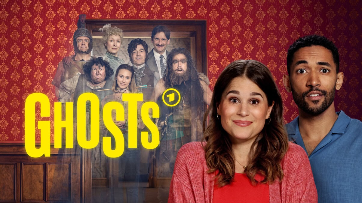 Großer gelber Schriftzug "GHOSTS" mit dem Logo von DAS ERSTE. dahinter stehen sieben Personen, die Kleider aus verschiedenen historischen Epochen tragen. Die Personen sehen transparent aus. Auf der rechten Seite stehen die beiden Hauptfiguren, ein Paar, das freundlich, aber etwas verwirrt in die Kamera sieht.