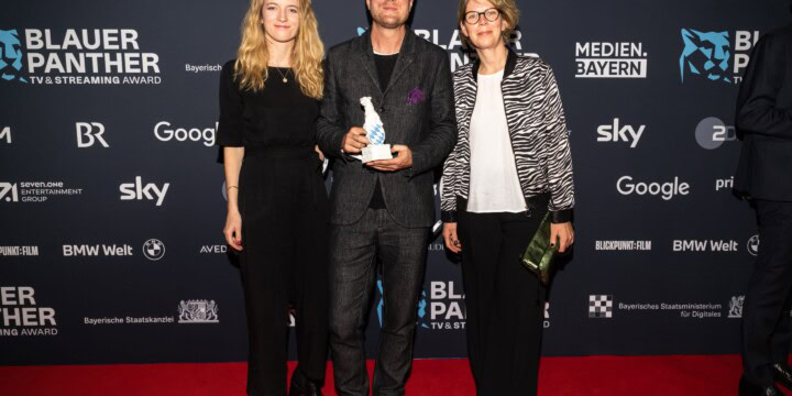 Preisträger Carl Gierstorfer (in der Mitte) mit Mareike Müller (Idee) und Antje Böhmert (Produktion) vor der Pressewand des Blauen Panthers 2022
