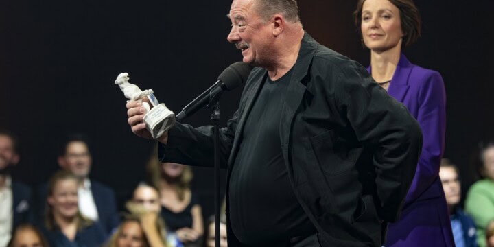 Peter Kurth mit dem Preis in der Hand, vor dem Mikrofon. Er hält gerade seine Dankesrede in der Show 2022.